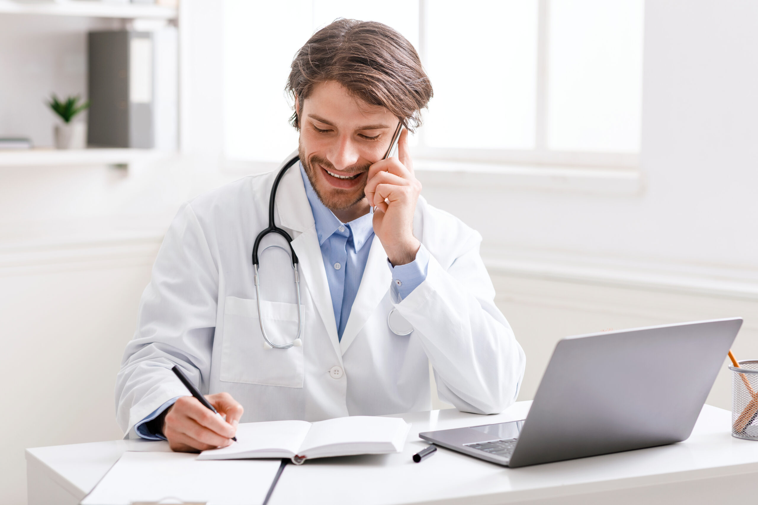 Friendly Doctor Talking With Patient Via Phone And Taking Notes,
